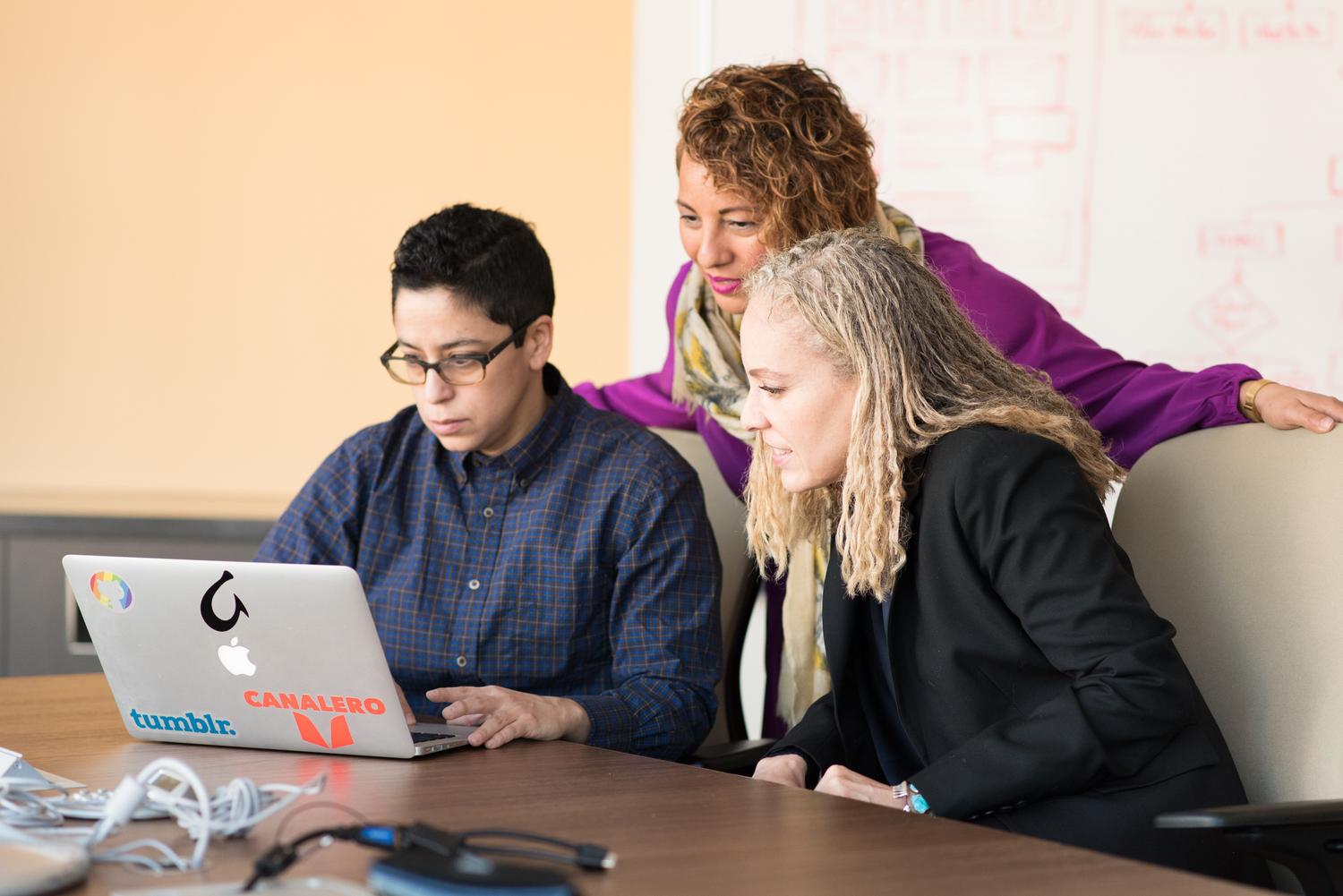 Tres personas de un equipo de trabajo colaborando frente a un portátil, ideal para representar la administración de software compartido.