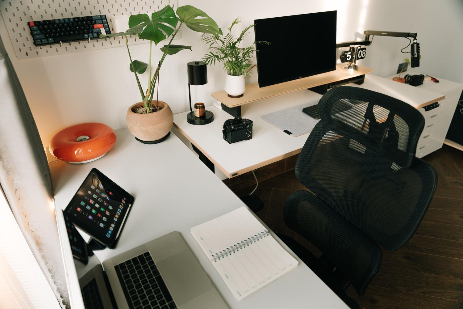Configuración de oficina en casa de alta gama con monitor ultrawide y tablet, representando la multitarea intensiva y la organización.