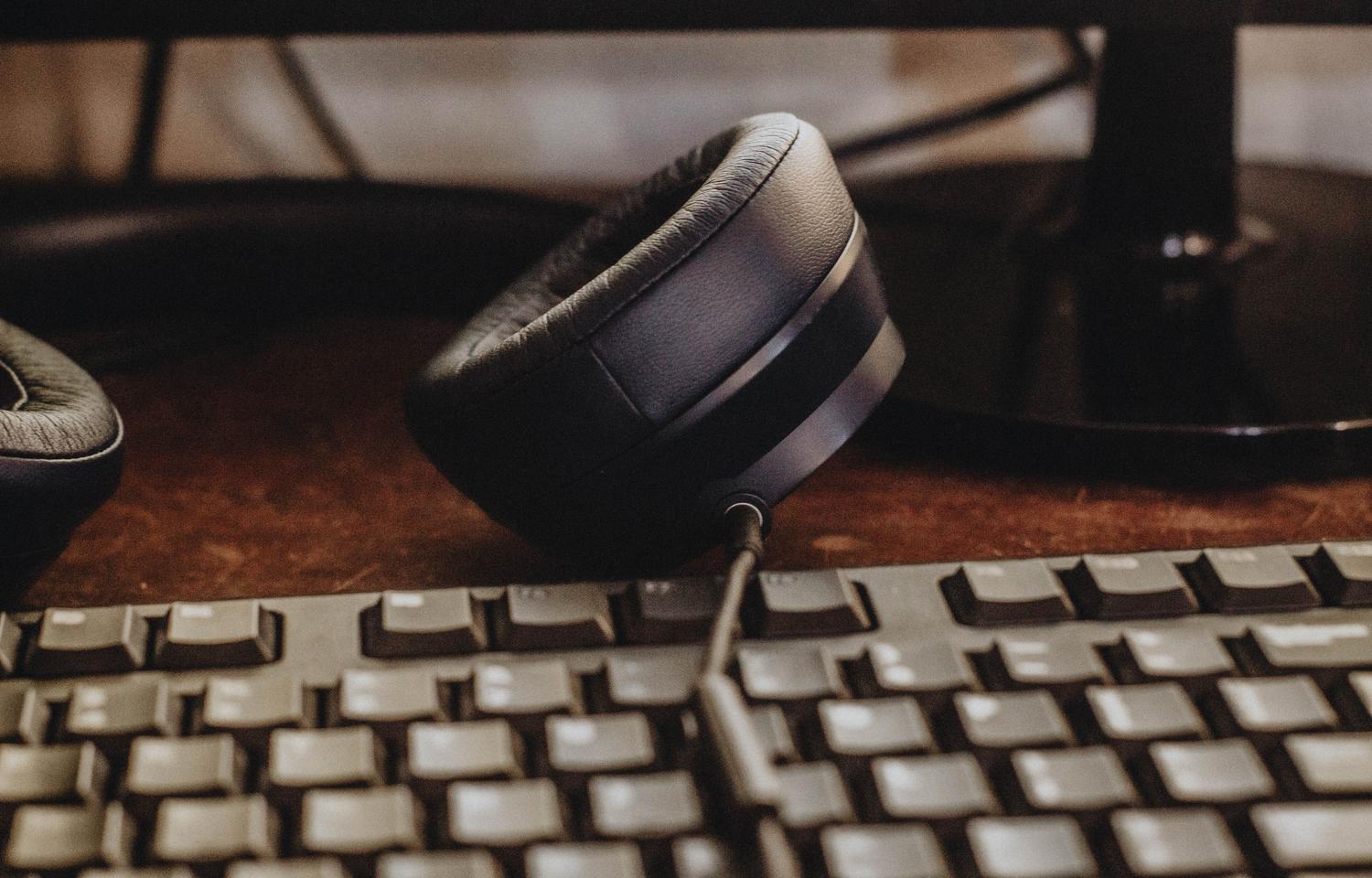 Auriculares y teclado mecánico sobre un escritorio de madera, representando un espacio de trabajo para audiófilos.