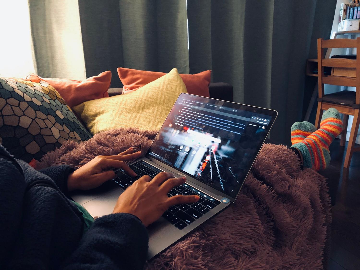 Persona descansando en un sofá cómodo utilizando un ordenador portátil para ver series y películas.