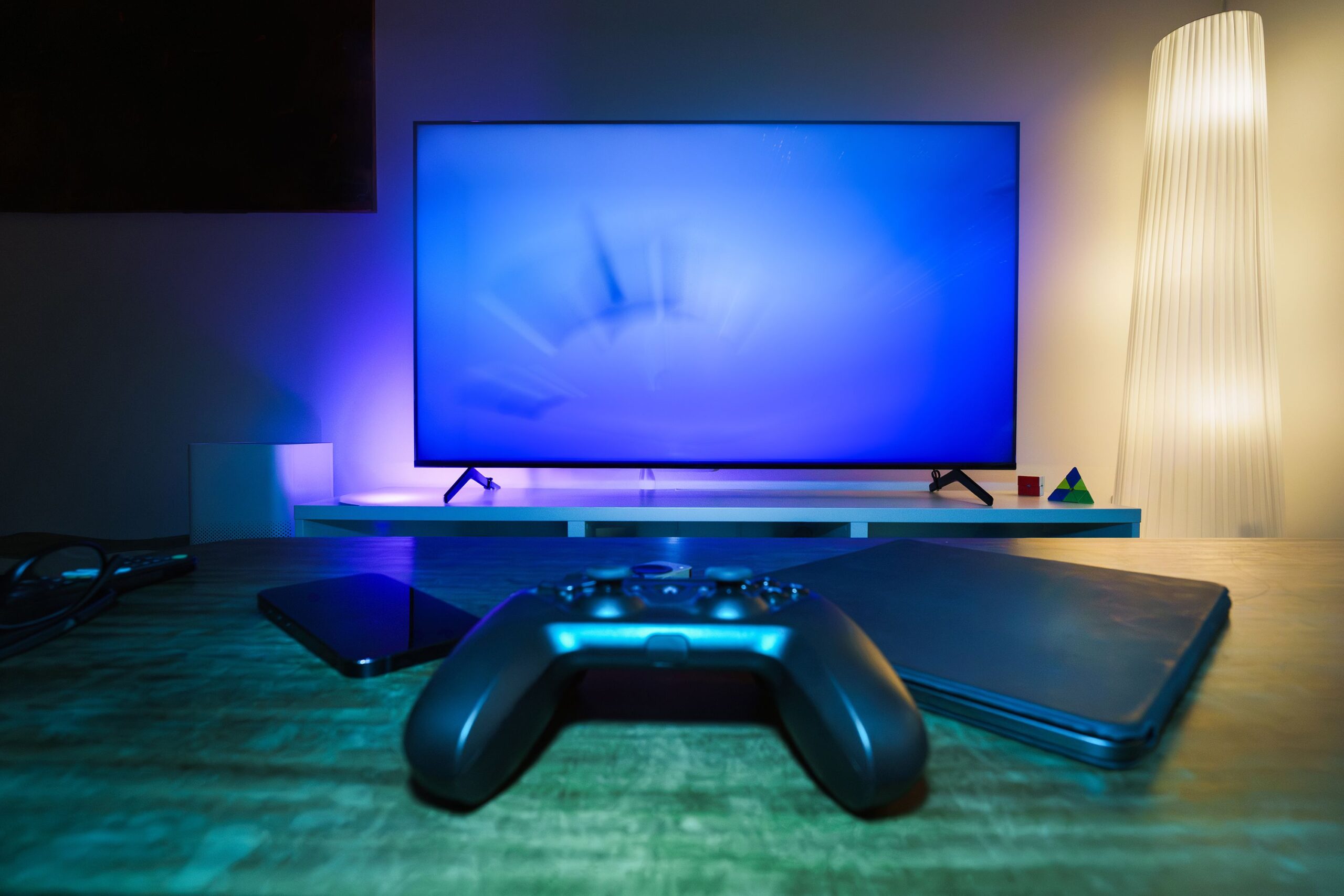 Setup moderno de cine en casa y gaming con Smart TV, mando de consola y luces ambientales azules.