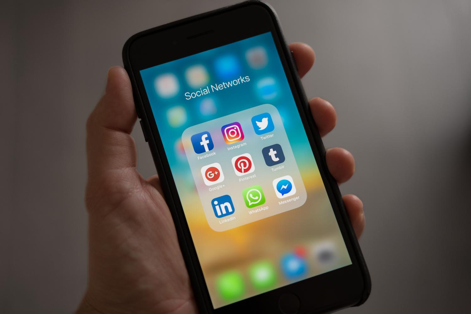 Mano sosteniendo un smartphone que muestra iconos de diversas redes sociales, representando el ecosistema de microcomunidades de Reddit.
