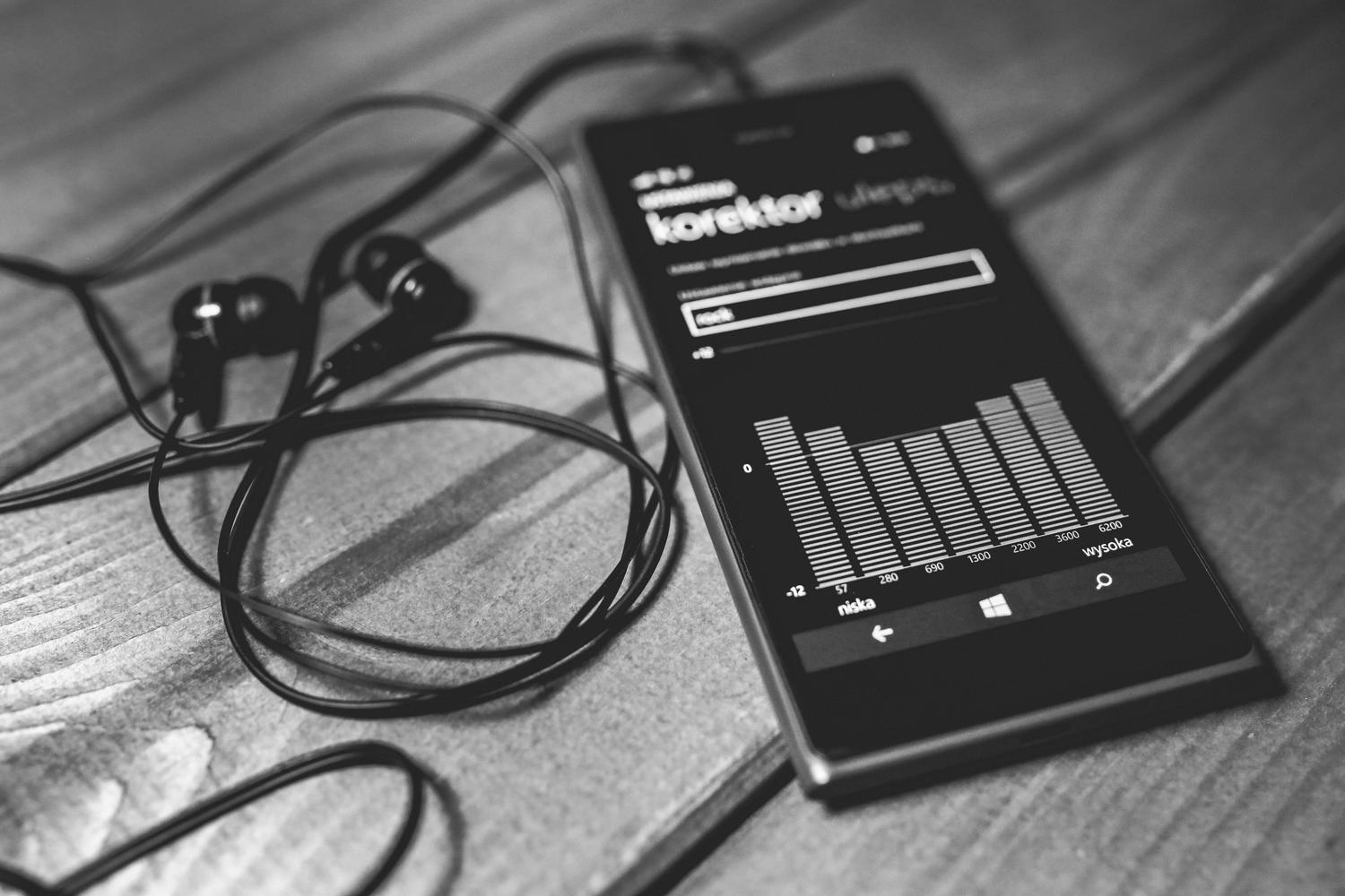 Primer plano de un smartphone mostrando un ecualizador de audio en la pantalla junto a unos auriculares