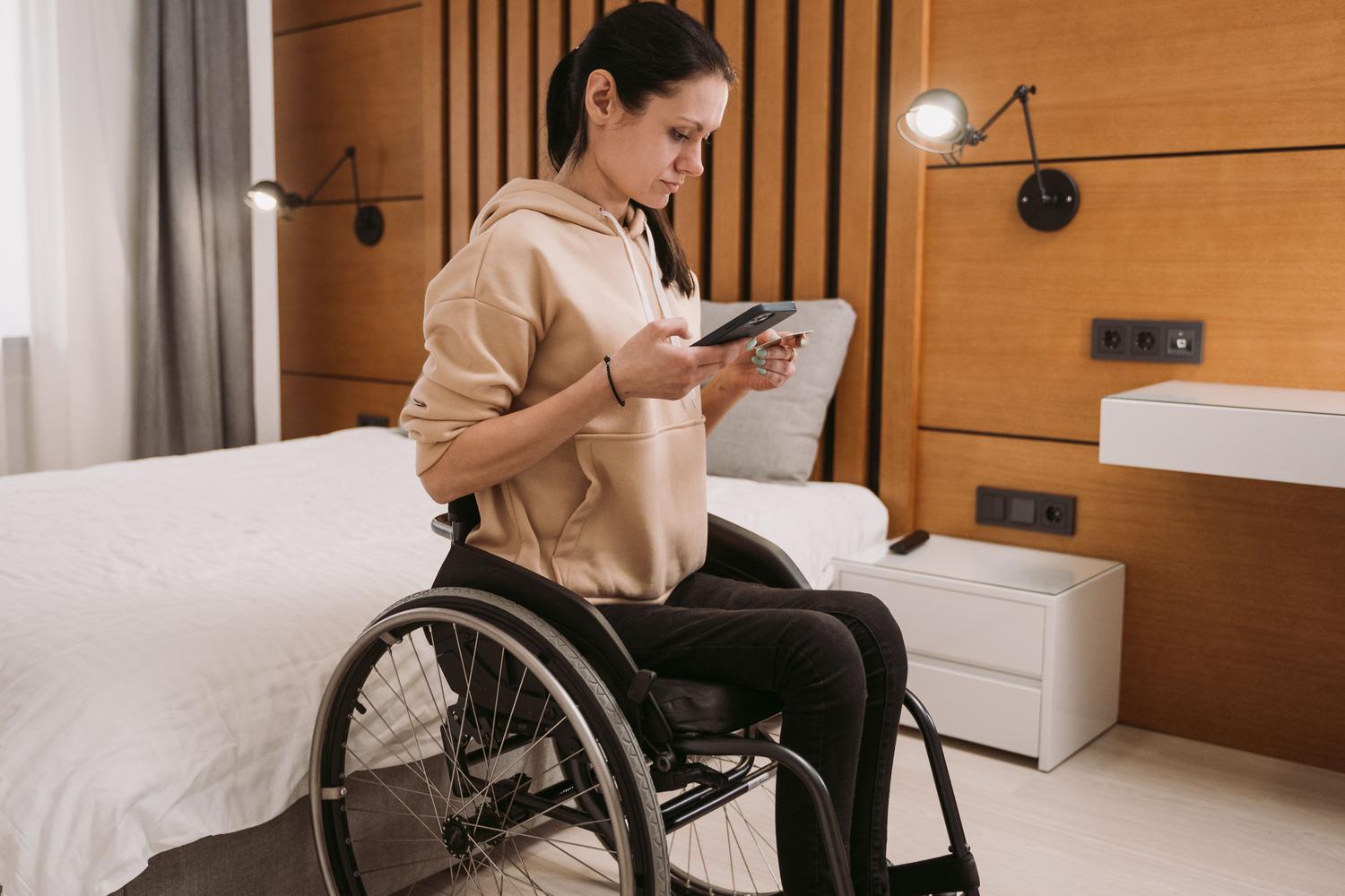 Mujer en silla de ruedas navegando por su smartphone en un dormitorio, representando la autonomía personal.