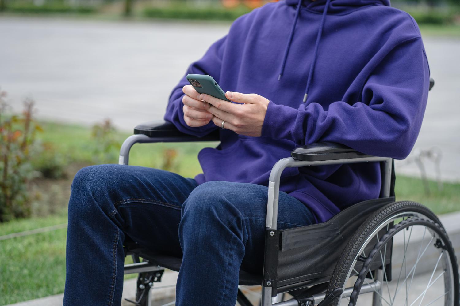 Persona en silla de ruedas utilizando un smartphone al aire libre para gestionar sus tareas diarias.