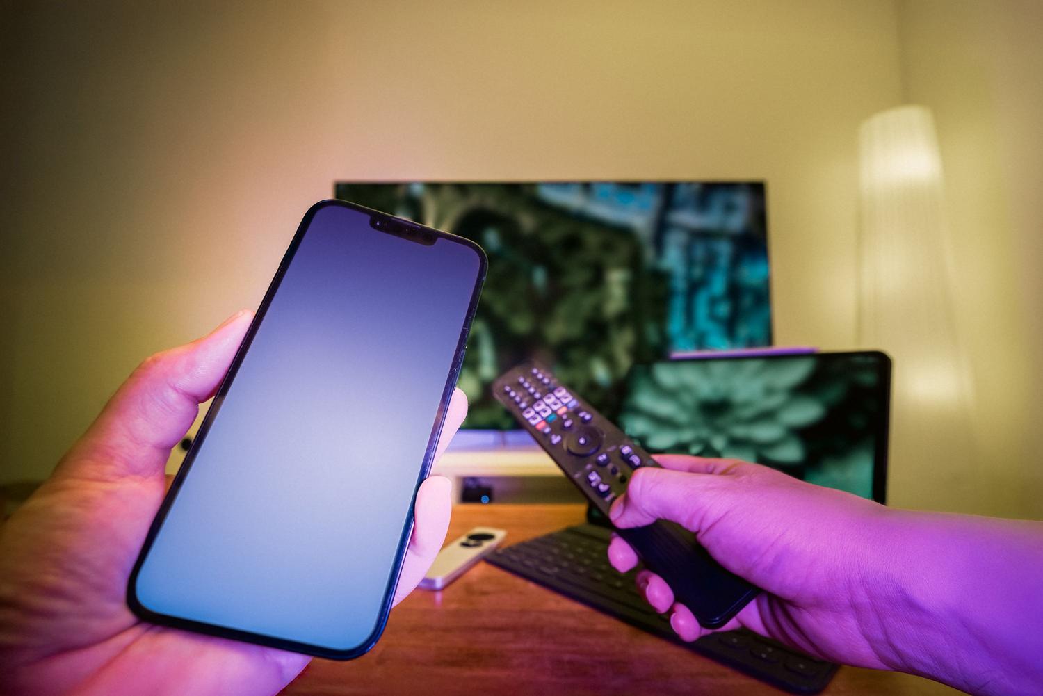 Manos sosteniendo un smartphone y un mando a distancia, ilustrando la gestión simultánea de la red de datos y el dispositivo de televisión.