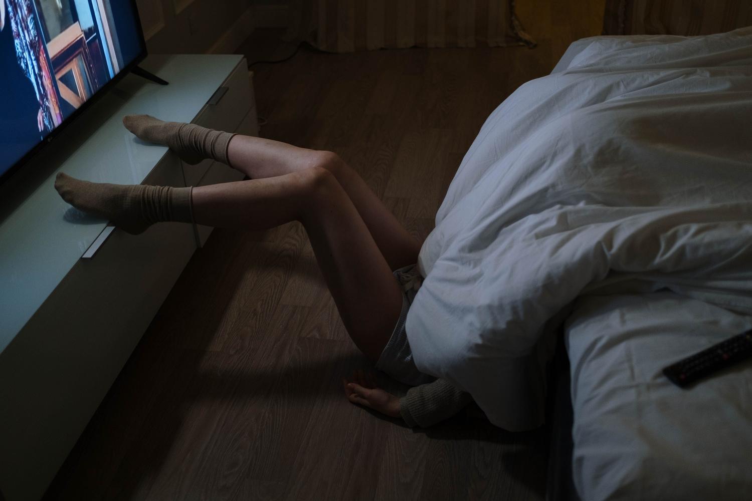 Persona viendo la televisión en un dormitorio tenuemente iluminado, resaltando el contraste de brillo de la pantalla.