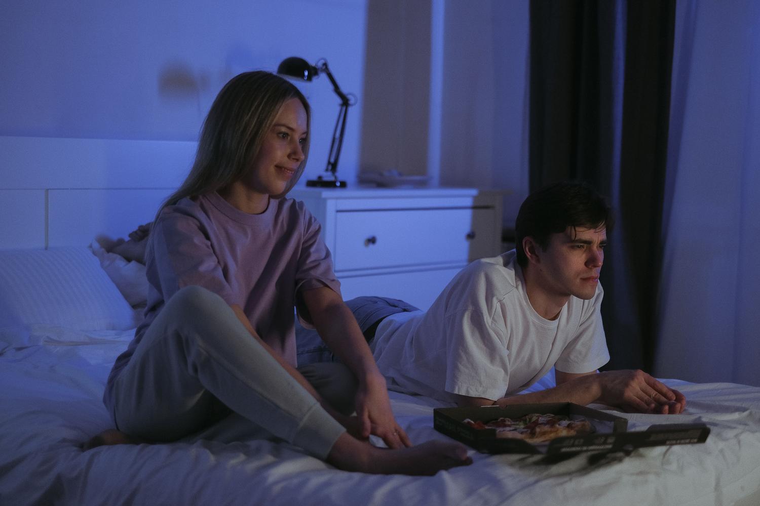 Pareja joven relajada en la cama viendo la televisión por la noche en un ambiente acogedor.
