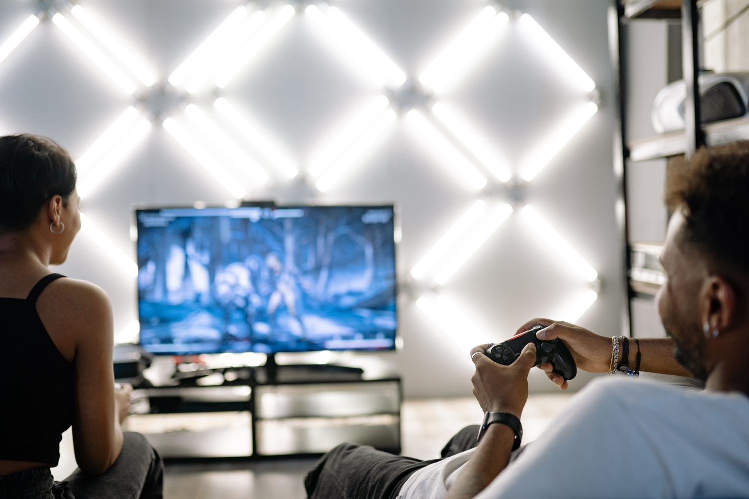 Dos personas jugando videojuegos en un salón moderno con paneles de luz LED decorativos.