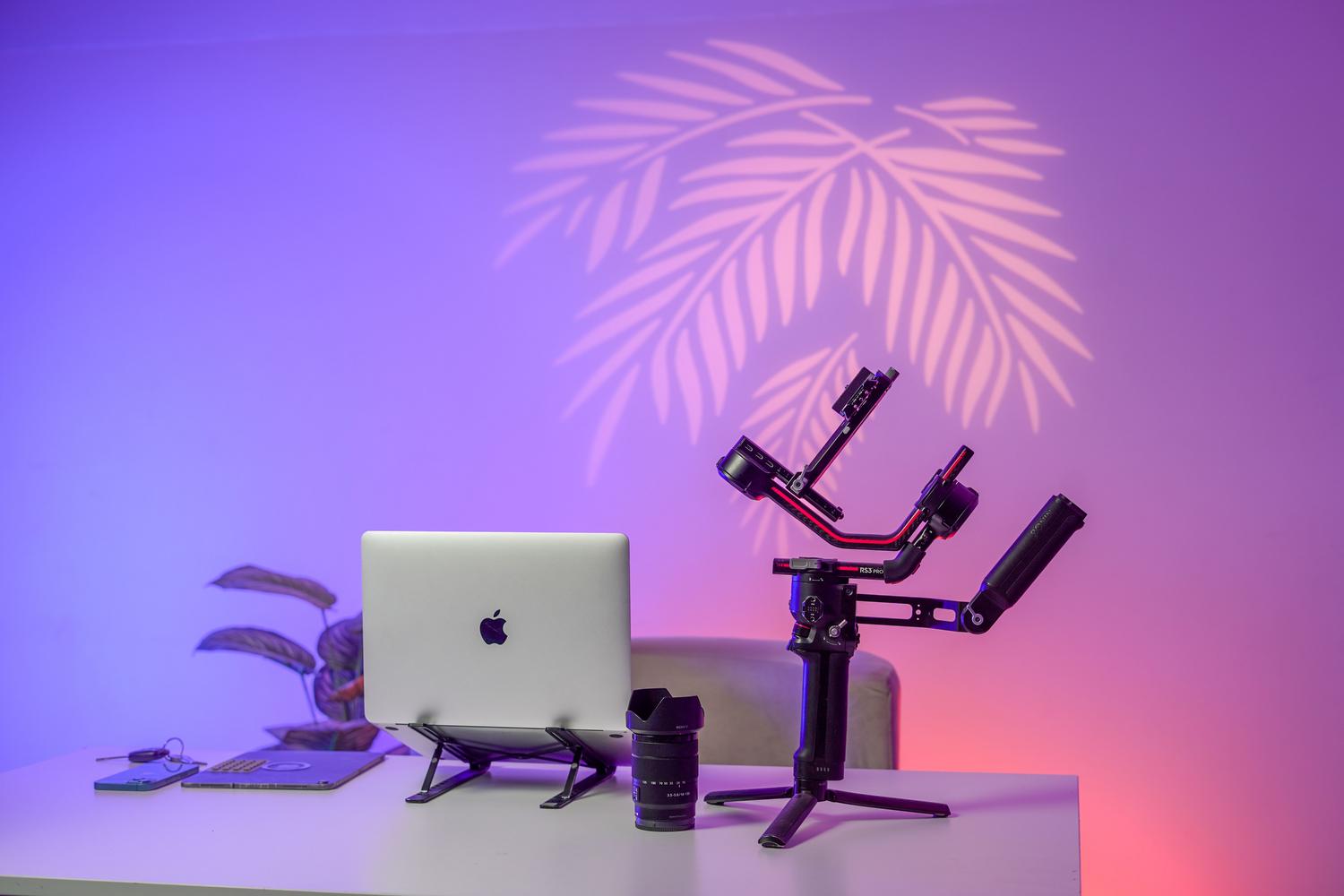 Setup de escritorio moderno con MacBook Pro, gimbal y lentes de cámara, ilustrando el hardware necesario para la producción de vídeo.