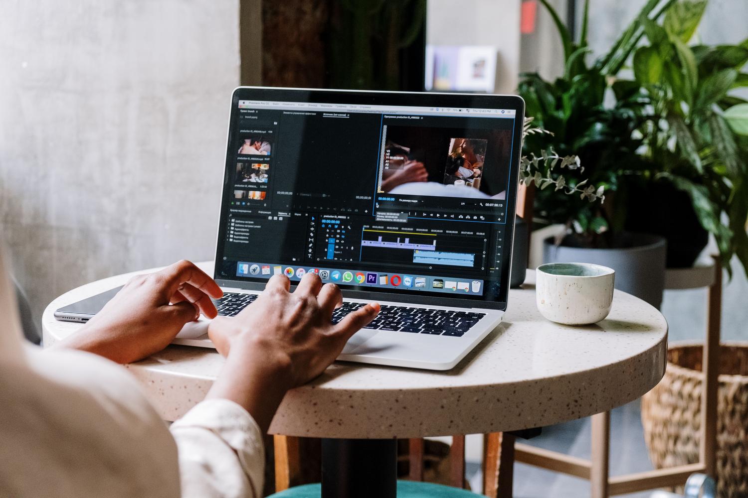 Persona editando vídeo en un MacBook Pro en un entorno de oficina moderna o cafetería, representando al profesional creativo.