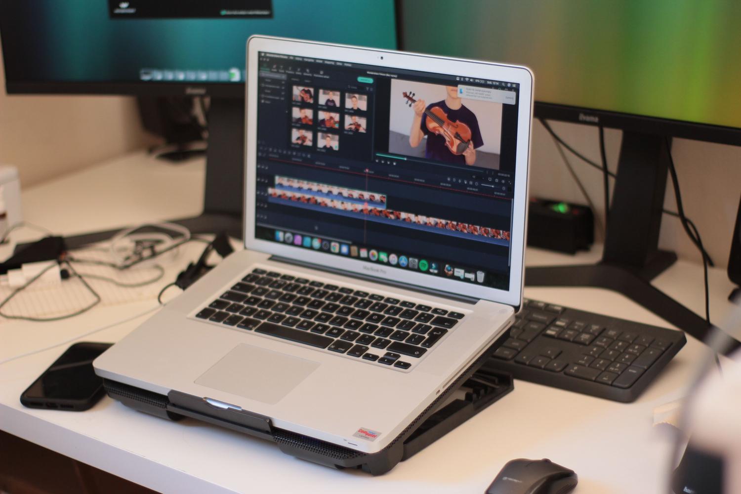 Espacio de trabajo profesional con MacBook Pro sobre soporte, monitores externos y software de edición de vídeo activo.