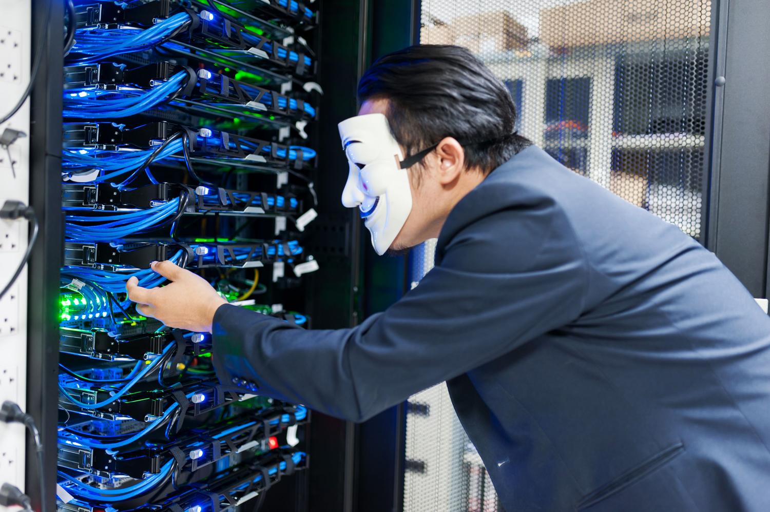 Masked individual interacting with server racks, symbolizing potential cybersecurity and physical security threats.
