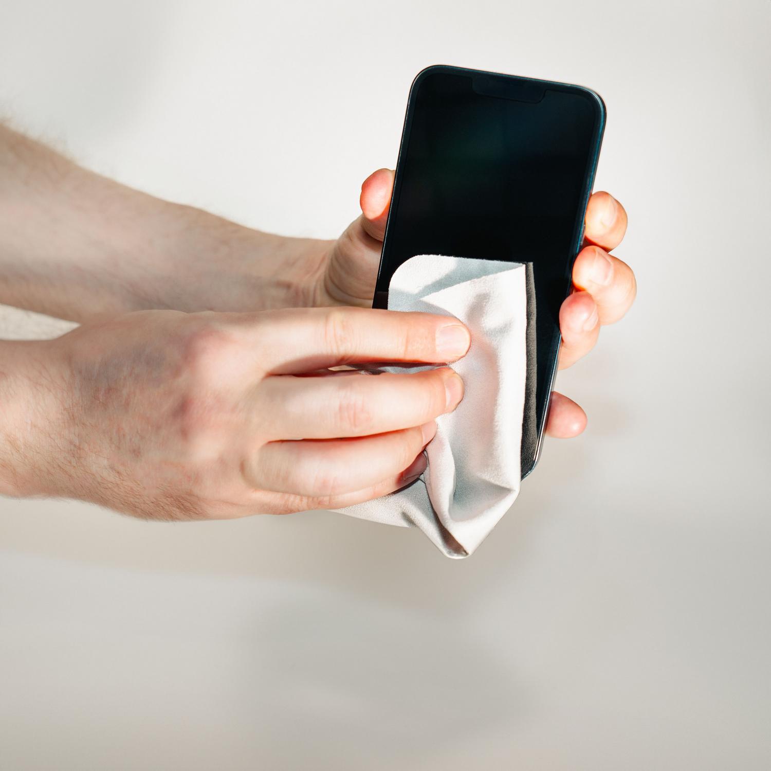 Persona limpiando la pantalla de un smartphone con un paño de microfibra para eliminar suciedad y huellas.