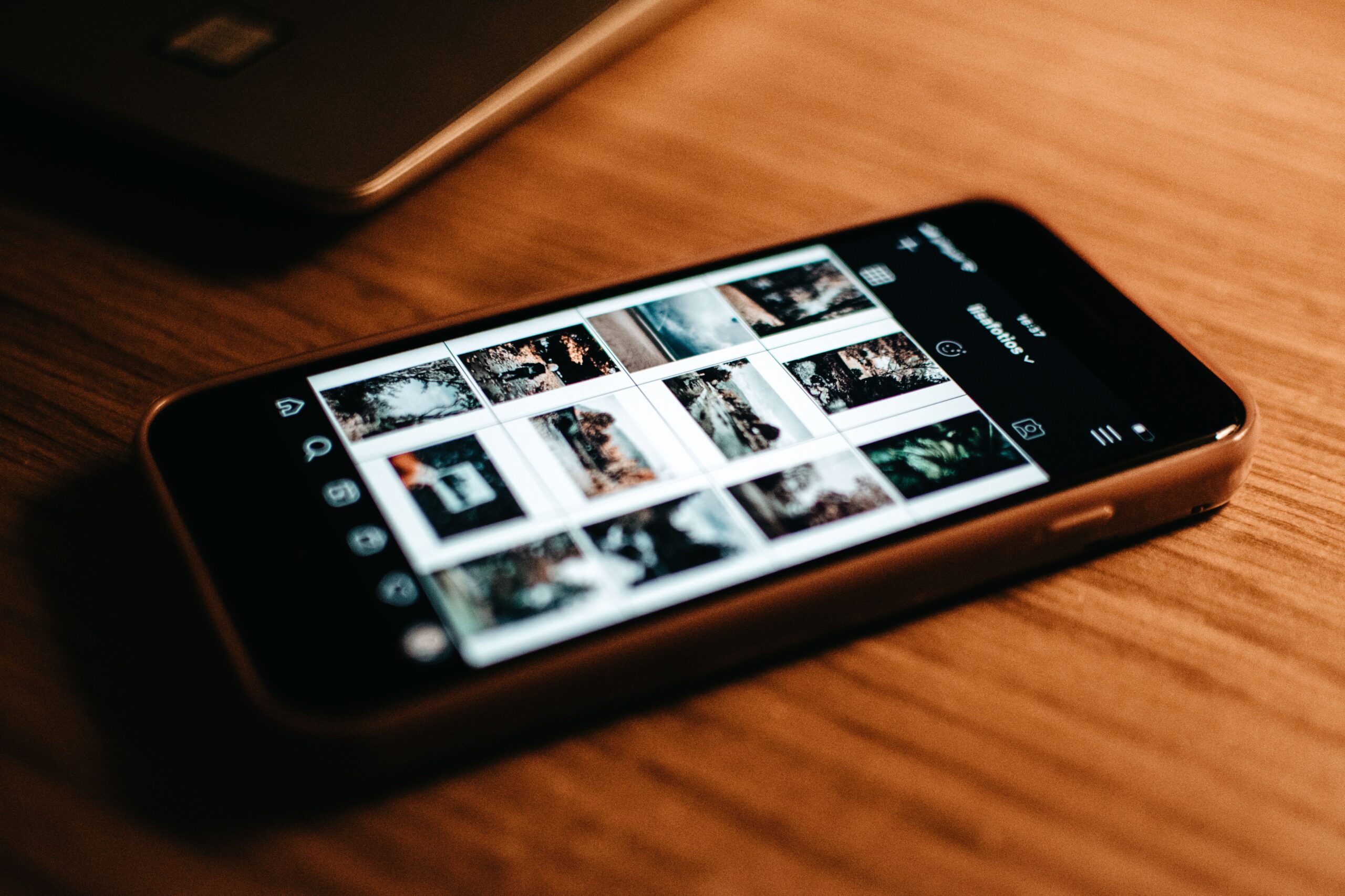 Smartphone mostrando una galería de fotos organizada en cuadrícula sobre una mesa de madera.