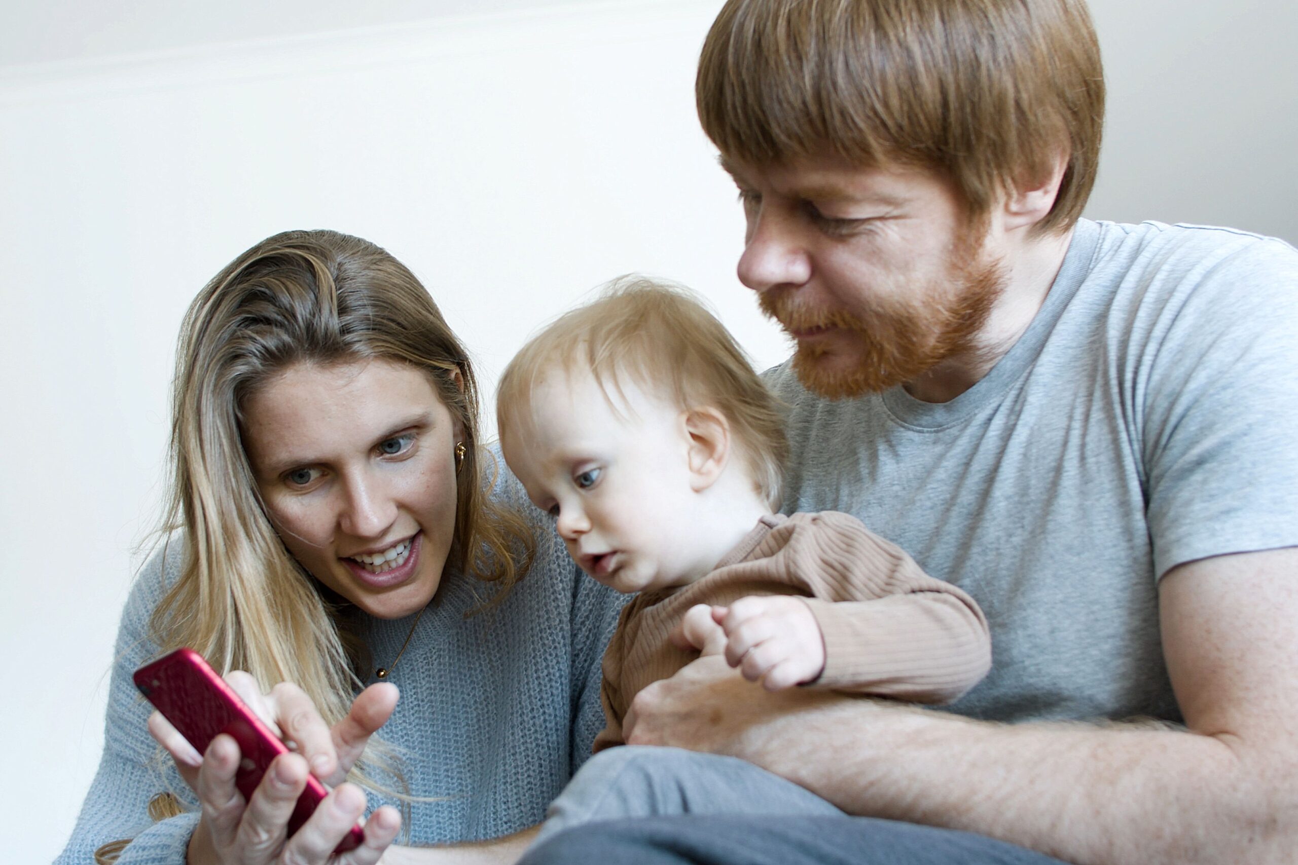 Familia joven compartiendo recuerdos mientras miran fotos en la pantalla de un teléfono móvil.