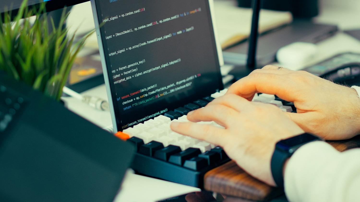 Desarrollador de software escribiendo código en un teclado mecánico, ilustrando la interacción entre el programador y las herramientas de automatización.