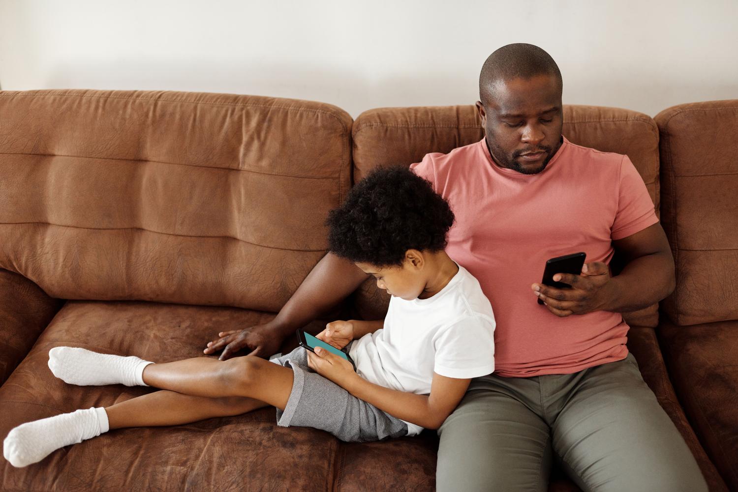 Padre e hijo utilizando smartphones juntos en el sofá, ilustrando la supervisión familiar y las herramientas de control parental.