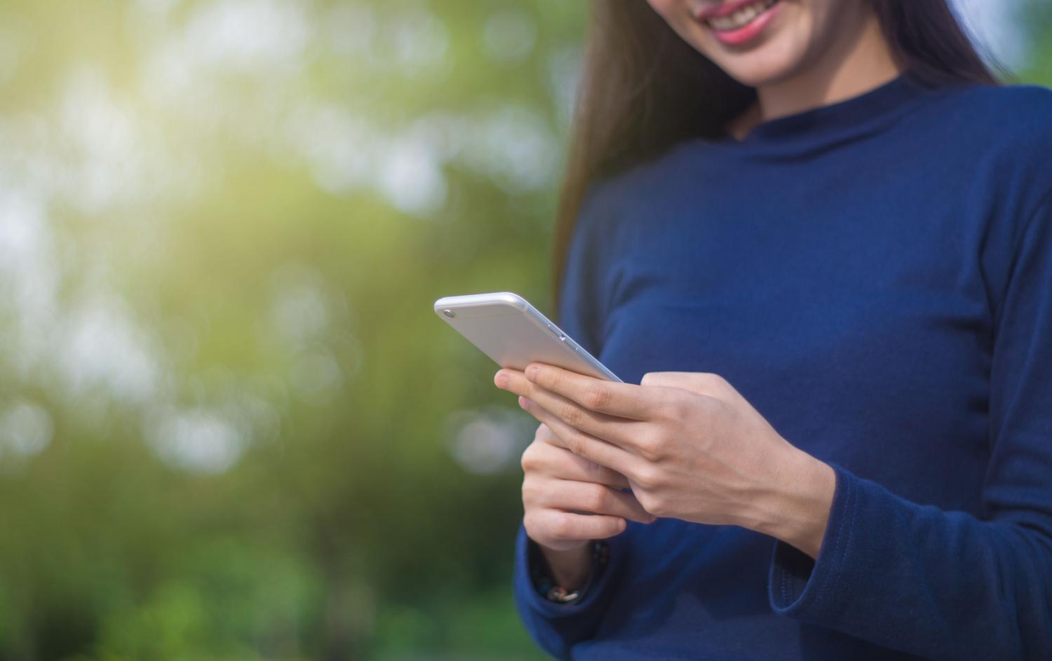 Persona utilizando un smartphone al aire libre, representando la interacción diaria con redes sociales y el consumo de contenido.