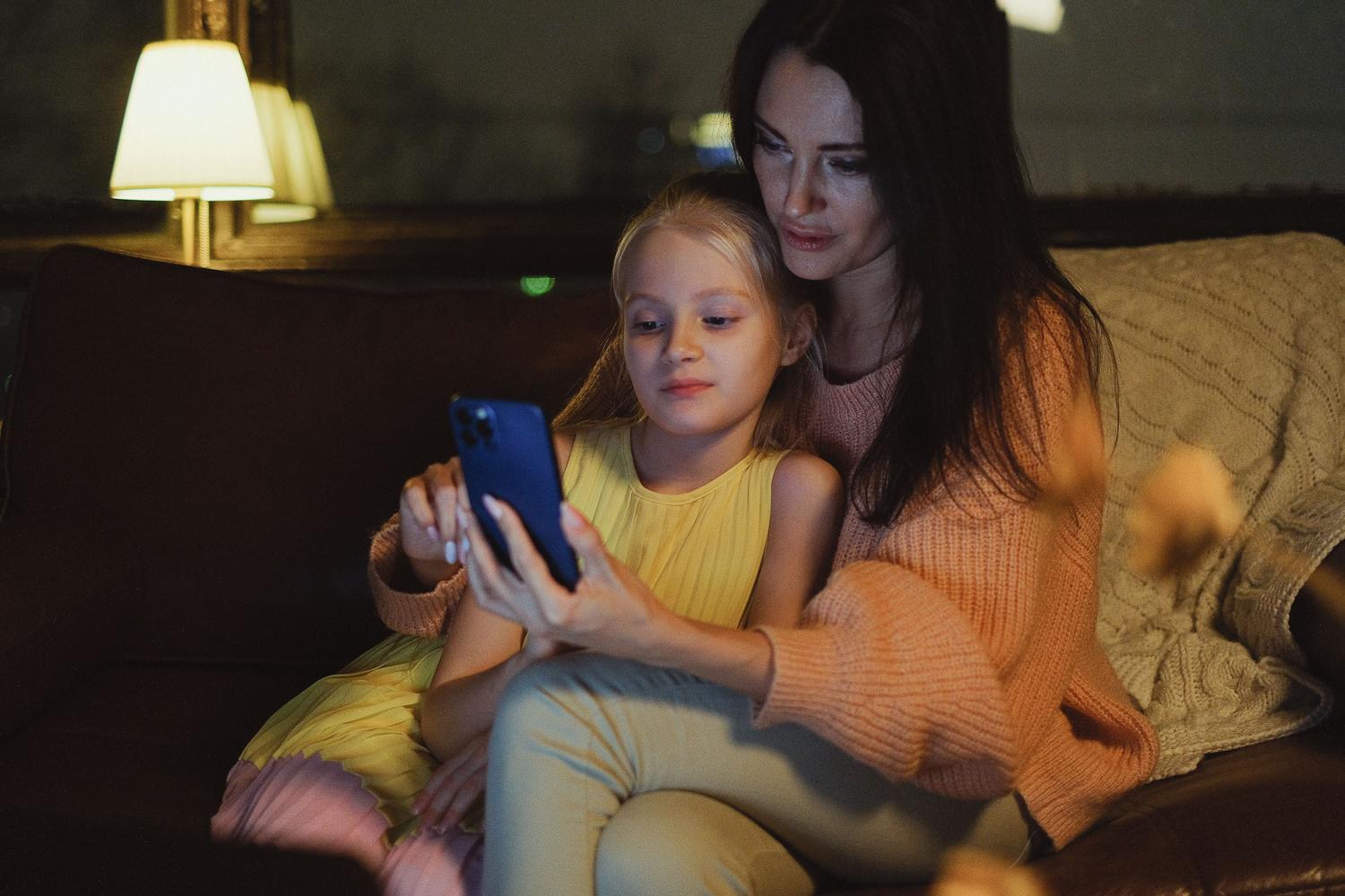 Madre e hija compartiendo la pantalla de un móvil en un ambiente acogedor, reflejando un entorno digital saludable.