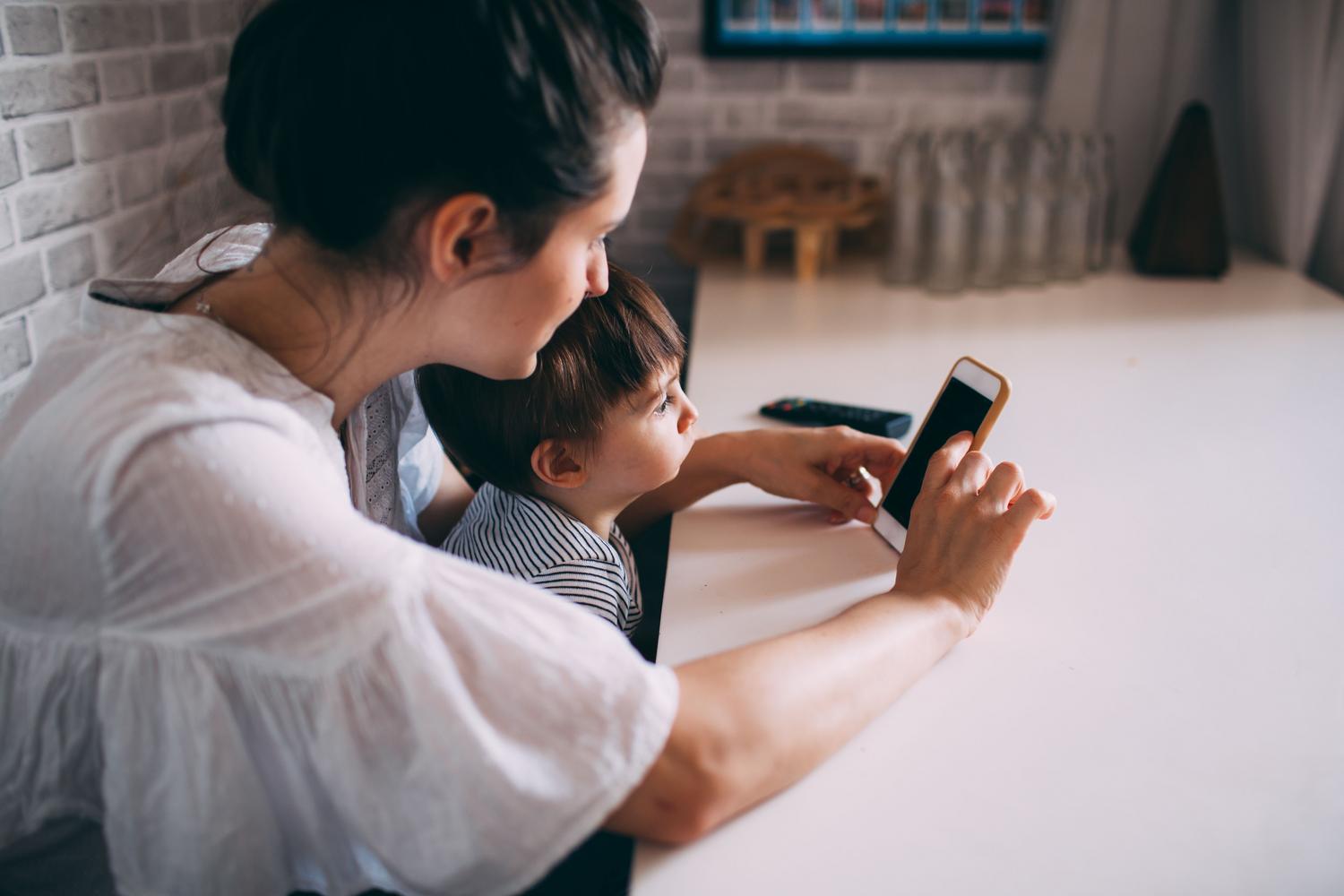 Una madre guiando a su hijo en el uso de un smartphone, representando la educación y supervisión digital.