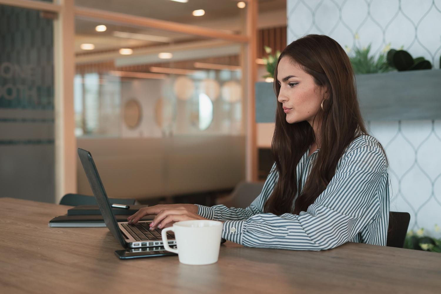 Mujer profesional concentrada trabajando en su portátil en una oficina luminosa, simbolizando la productividad individual.