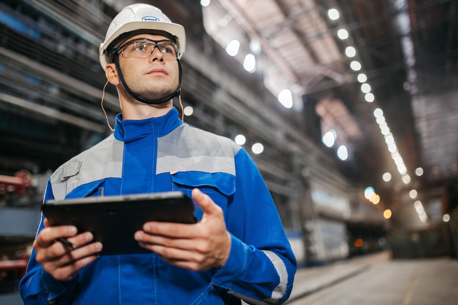 Operario industrial con equipo de seguridad utilizando una tablet en una fábrica moderna, ejemplificando las instrucciones de trabajo digitales.