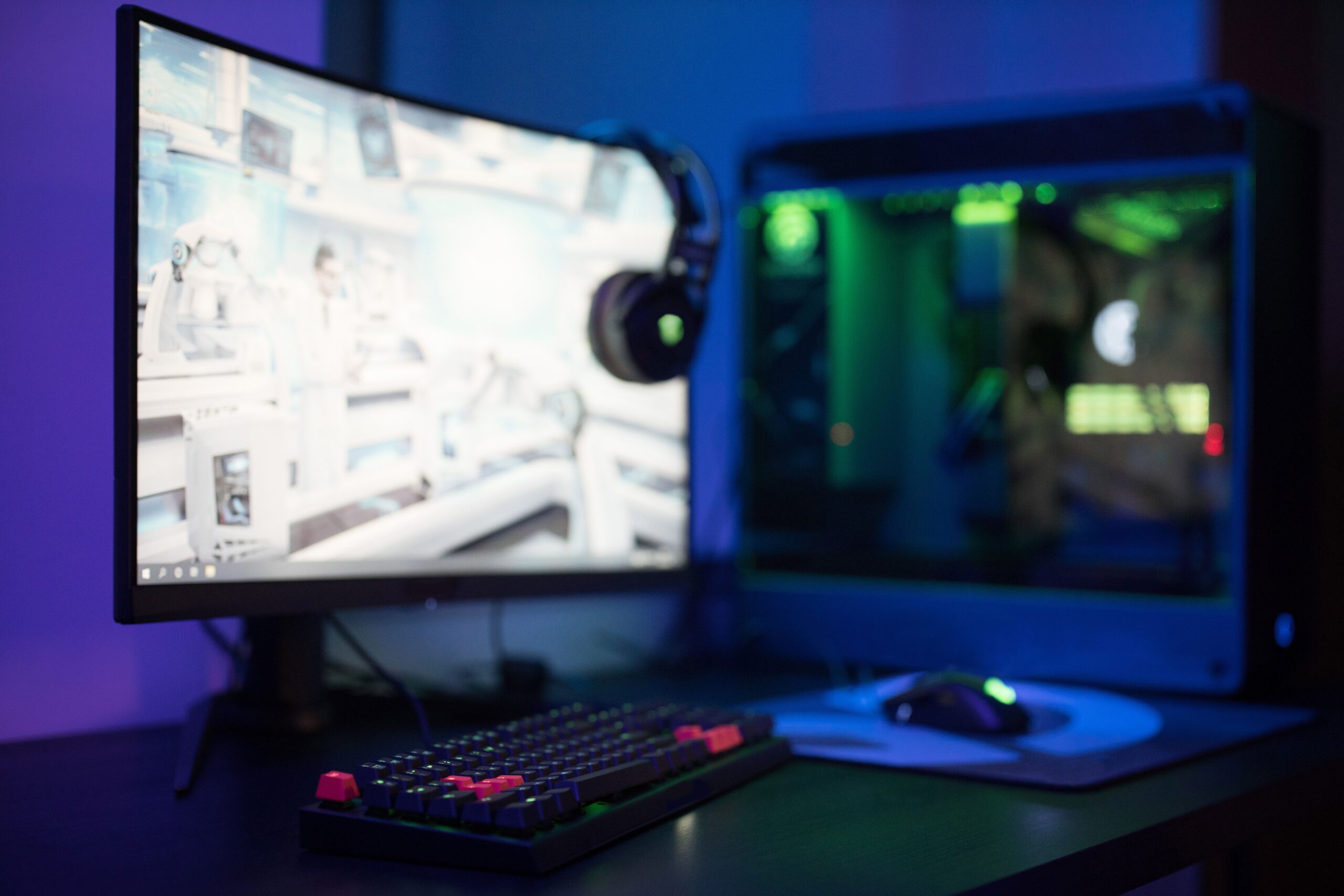 Setup gaming con monitor curvo y potente torre PC con luces RGB verdes, destacando la potencia gráfica y el rendimiento.