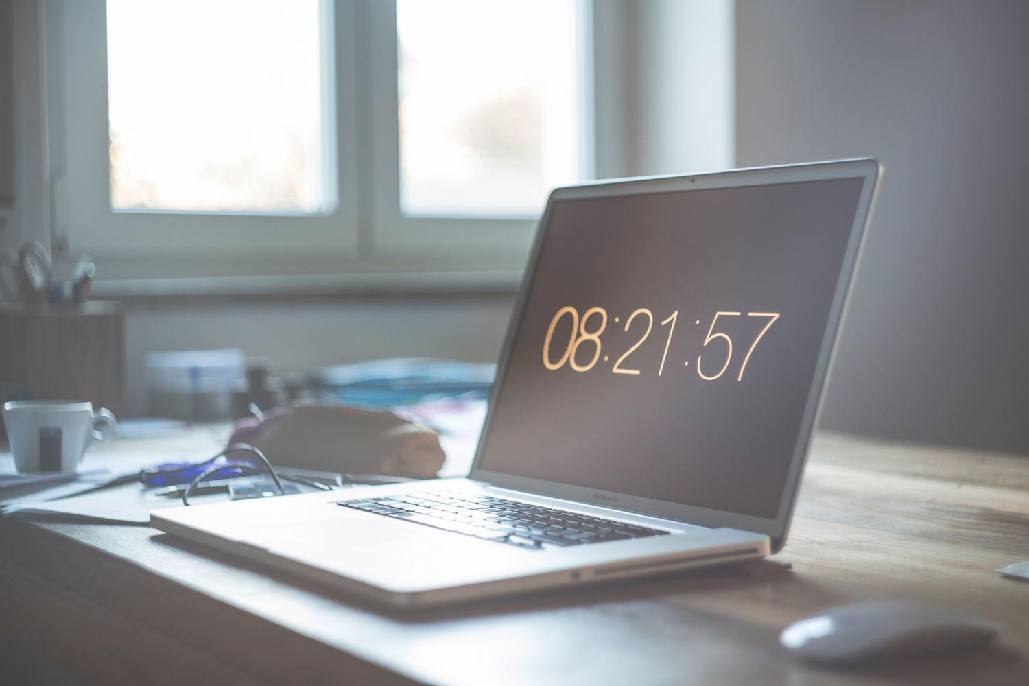 Laptop en un espacio de trabajo minimalista con un reloj digital en pantalla, simbolizando la gestión del tiempo.