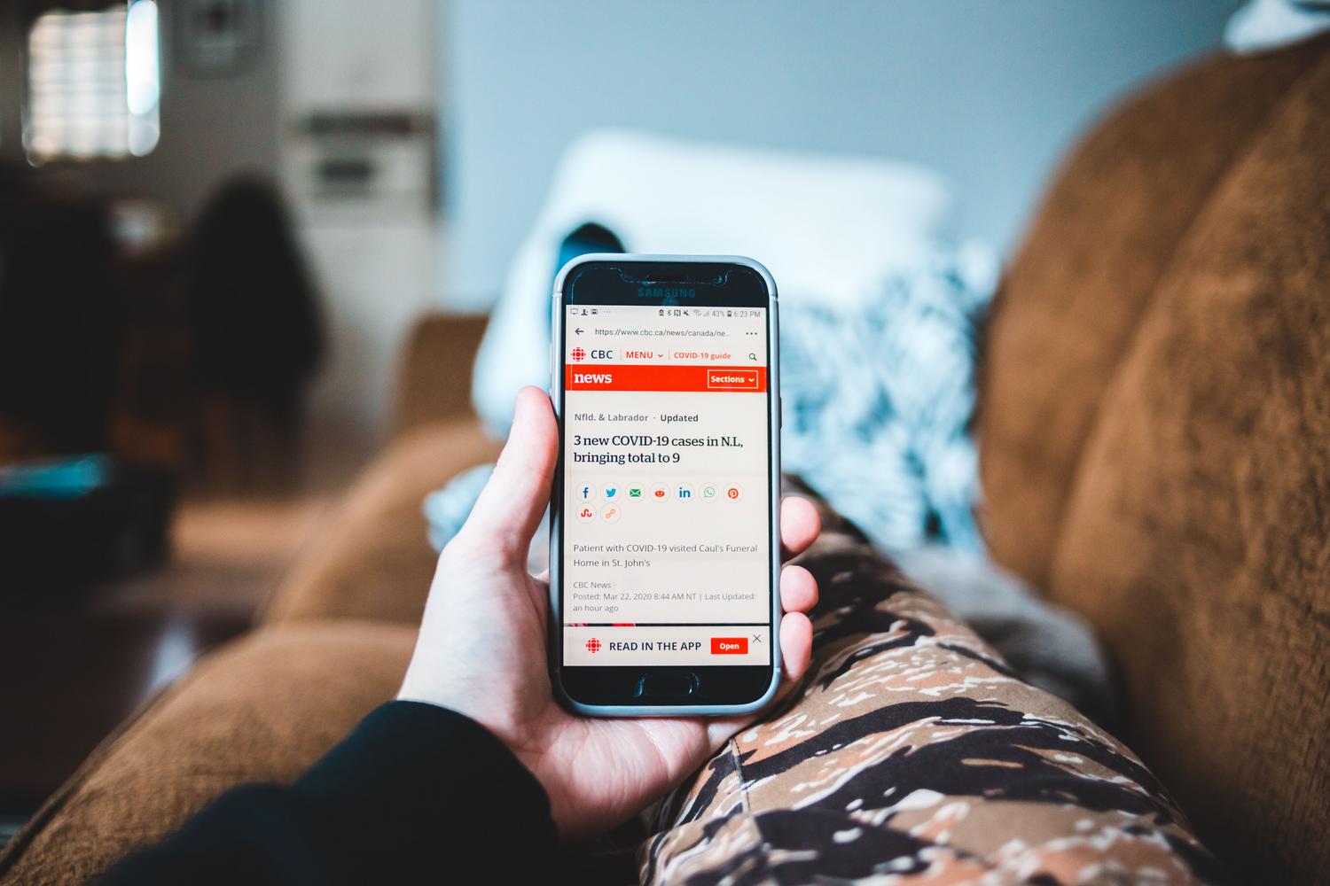 Persona relajada en un sofá leyendo noticias personalizadas en su smartphone.