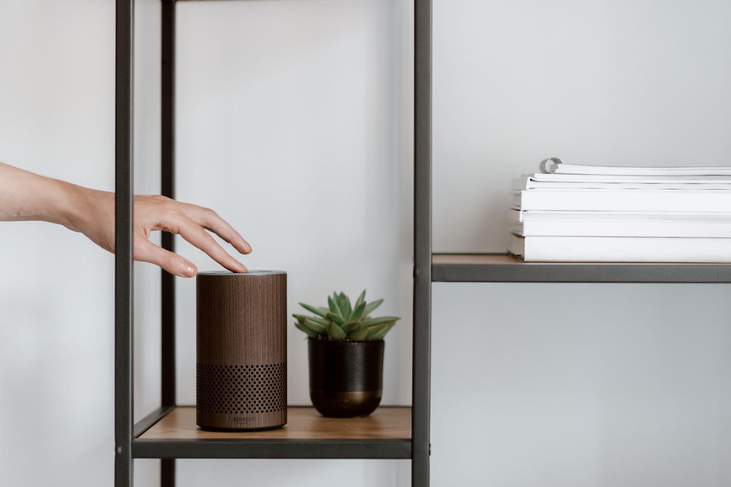 Mano ajustando la configuración de un altavoz inteligente en un estante minimalista.
