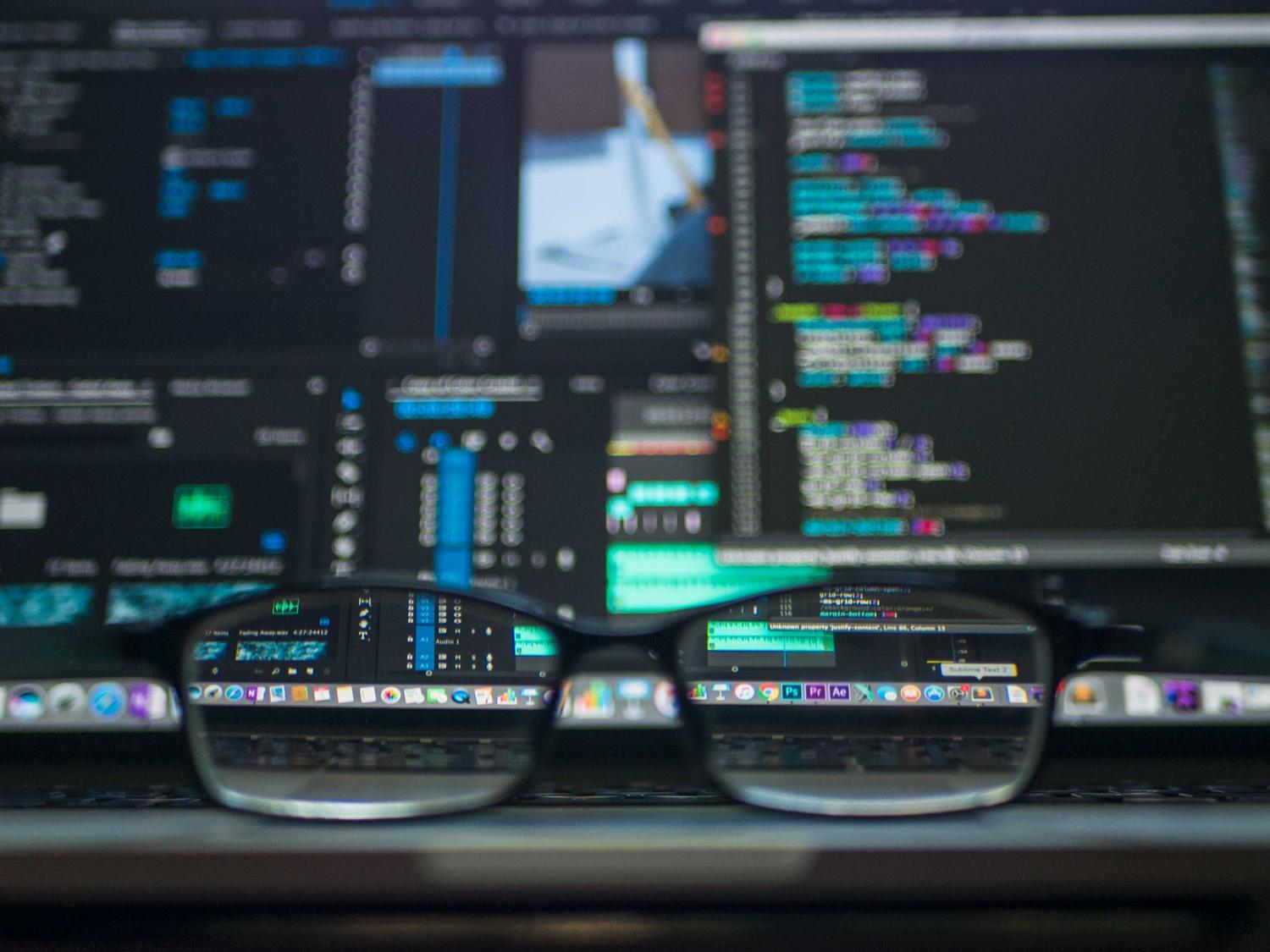 Gafas reflejando código de programación en un monitor, representando la configuración de identidad y el enfoque del desarrollador