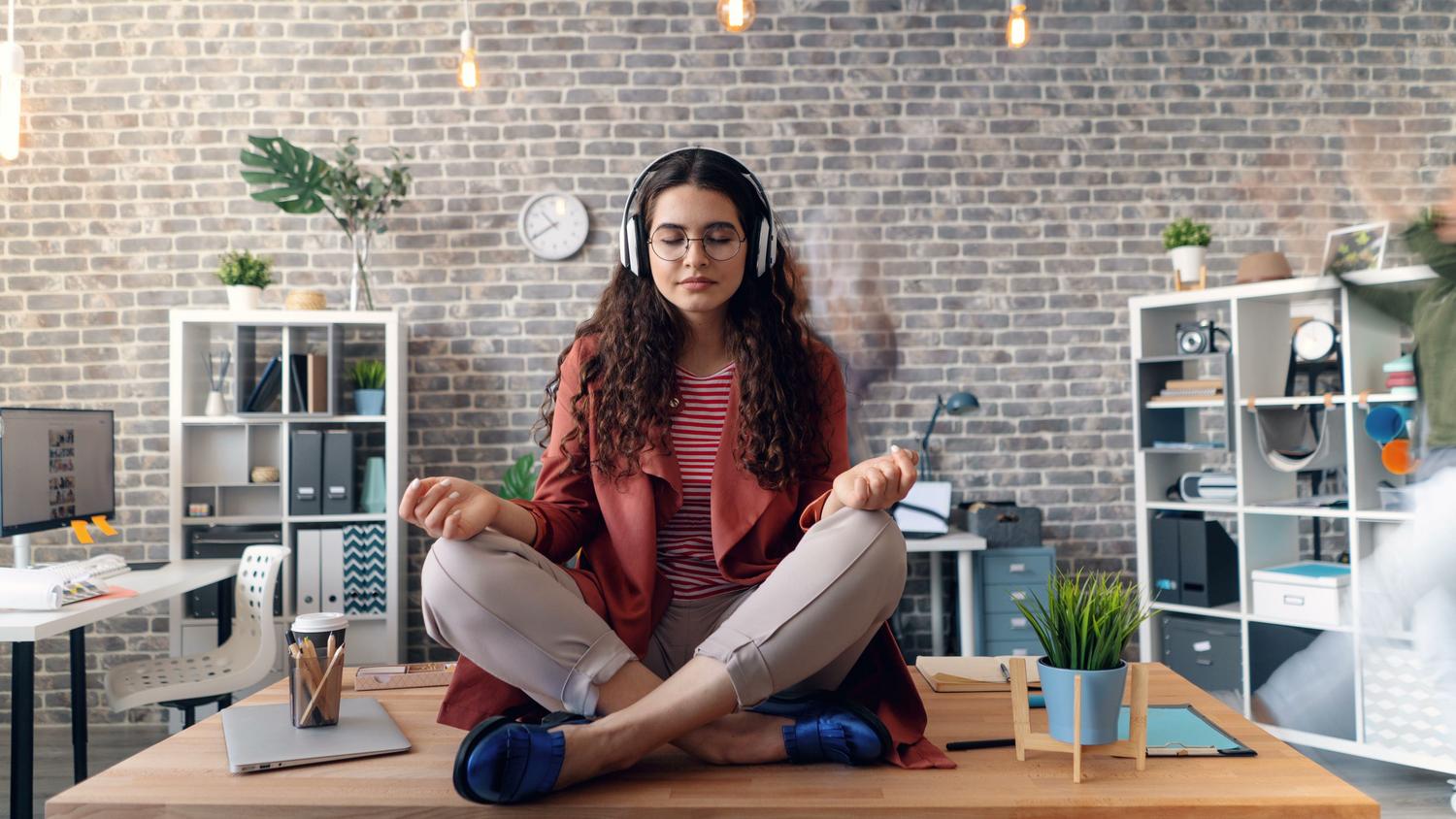 Una mujer practicando mindfulness y meditación con auriculares en una oficina moderna, ilustrando los modos de concentración Zen o Descanso.
