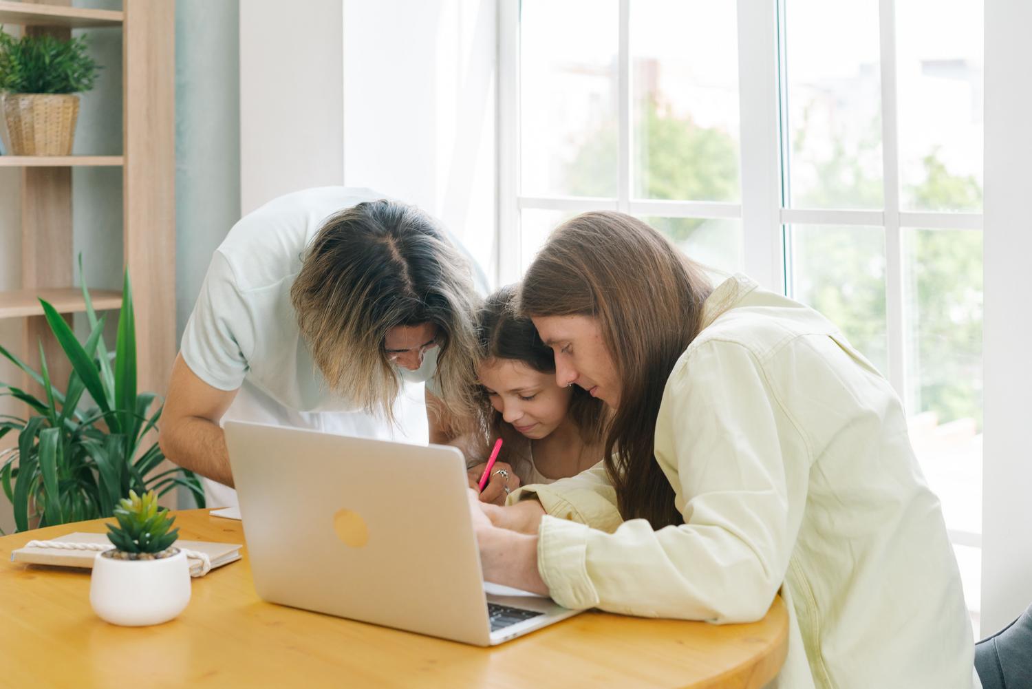 Padres ayudando a su hija con el ordenador, representando la supervisión y el control parental