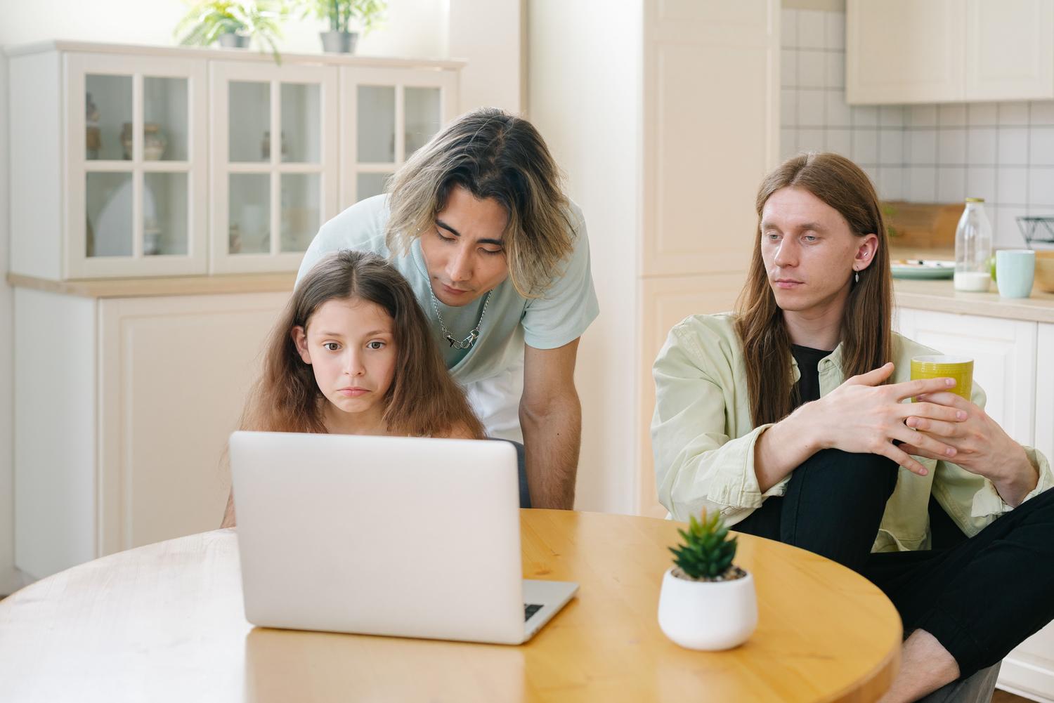 Adulto supervisando la navegación en internet de una niña en un ordenador compartido en la cocina