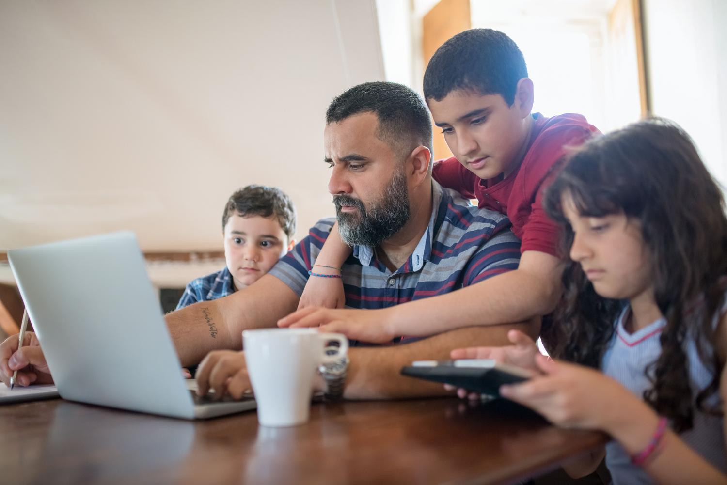 Padre supervisando la actividad digital de sus hijos mientras utilizan un portátil y una tableta en casa