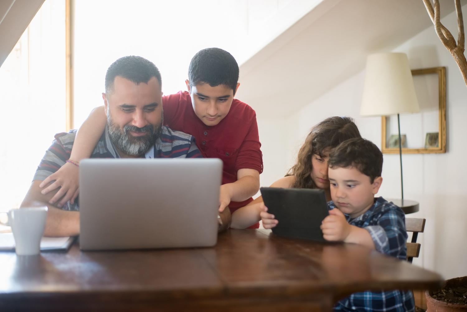 Padre e hijos compartiendo el uso de un ordenador portátil y una tableta en un ambiente familiar acogedor
