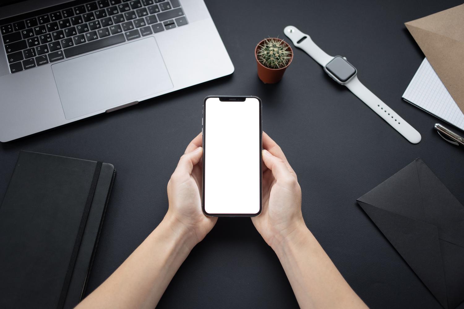 Manos sosteniendo un smartphone con pantalla en blanco sobre un escritorio minimalista, representando la configuración de aplicaciones de automatización.