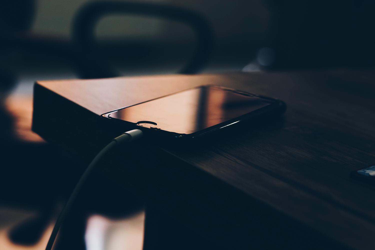 iPhone conectado a su cargador sobre una mesa de madera, mostrando una carga natural y cotidiana.