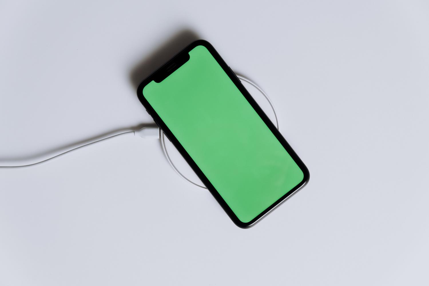 Smartphone sobre un cargador inalámbrico con pantalla verde, simbolizando una batería saludable y optimizada.