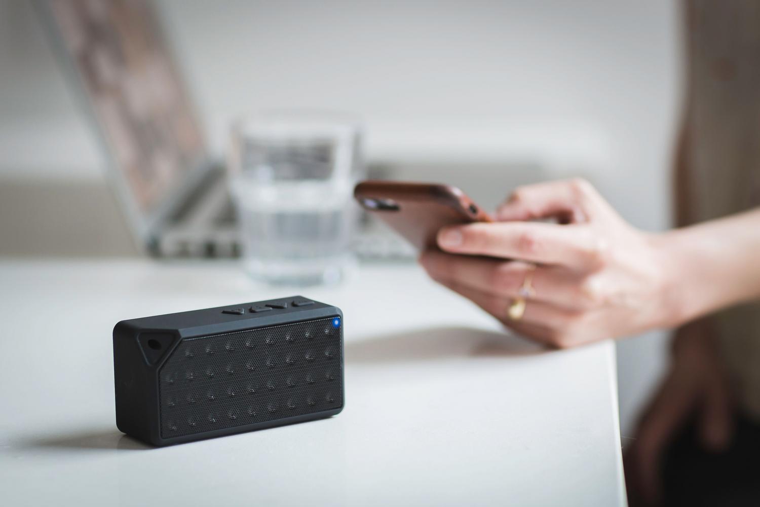 Uso de smartphone junto a dispositivo conectado en red local Persona utilizando un smartphone junto a un altavoz inalámbrico, ejemplificando la conectividad de red local.