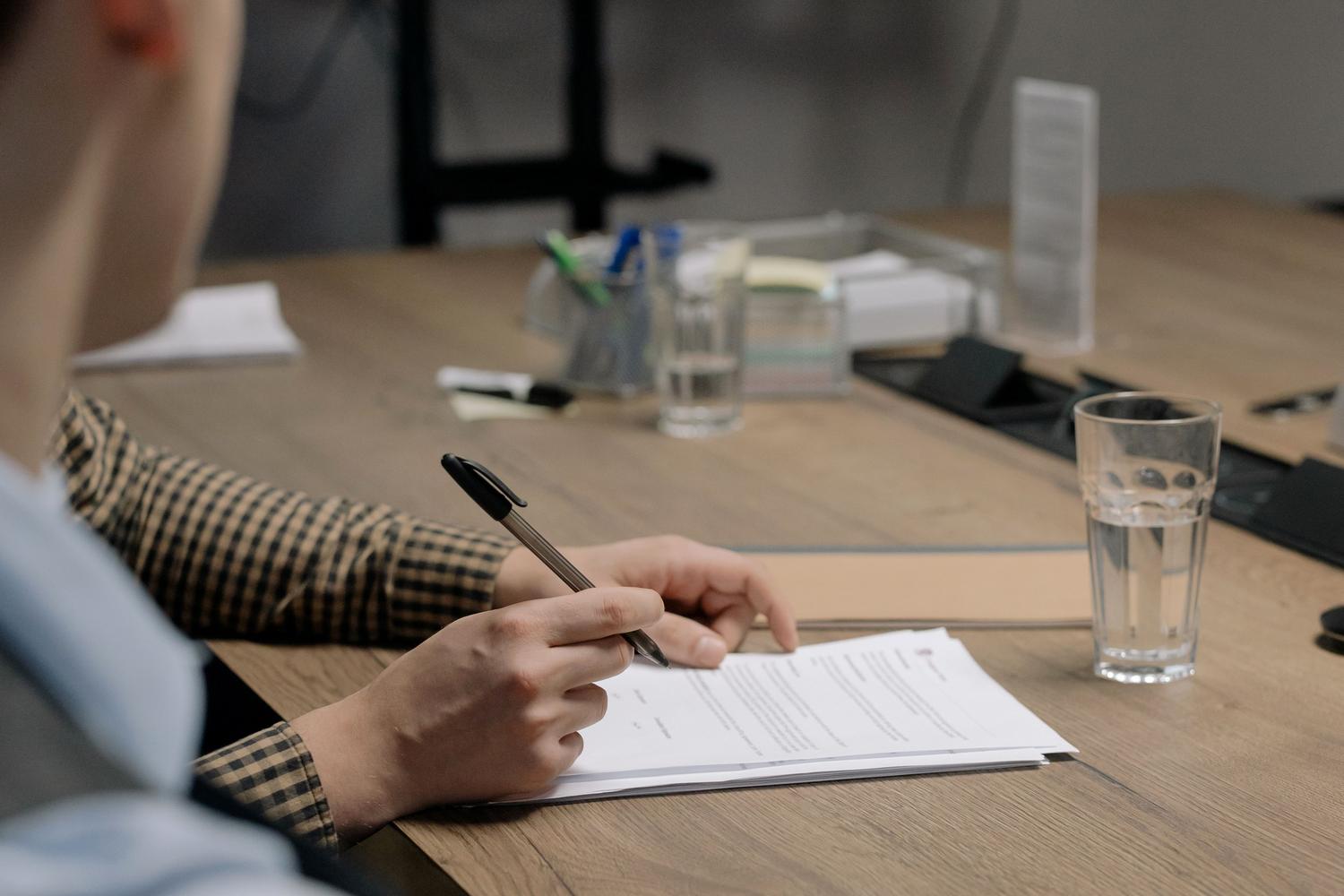 Una persona con vestimenta profesional firmando un contrato corporativo en una mesa de madera, ejemplificando la formalización de acuerdos legales.