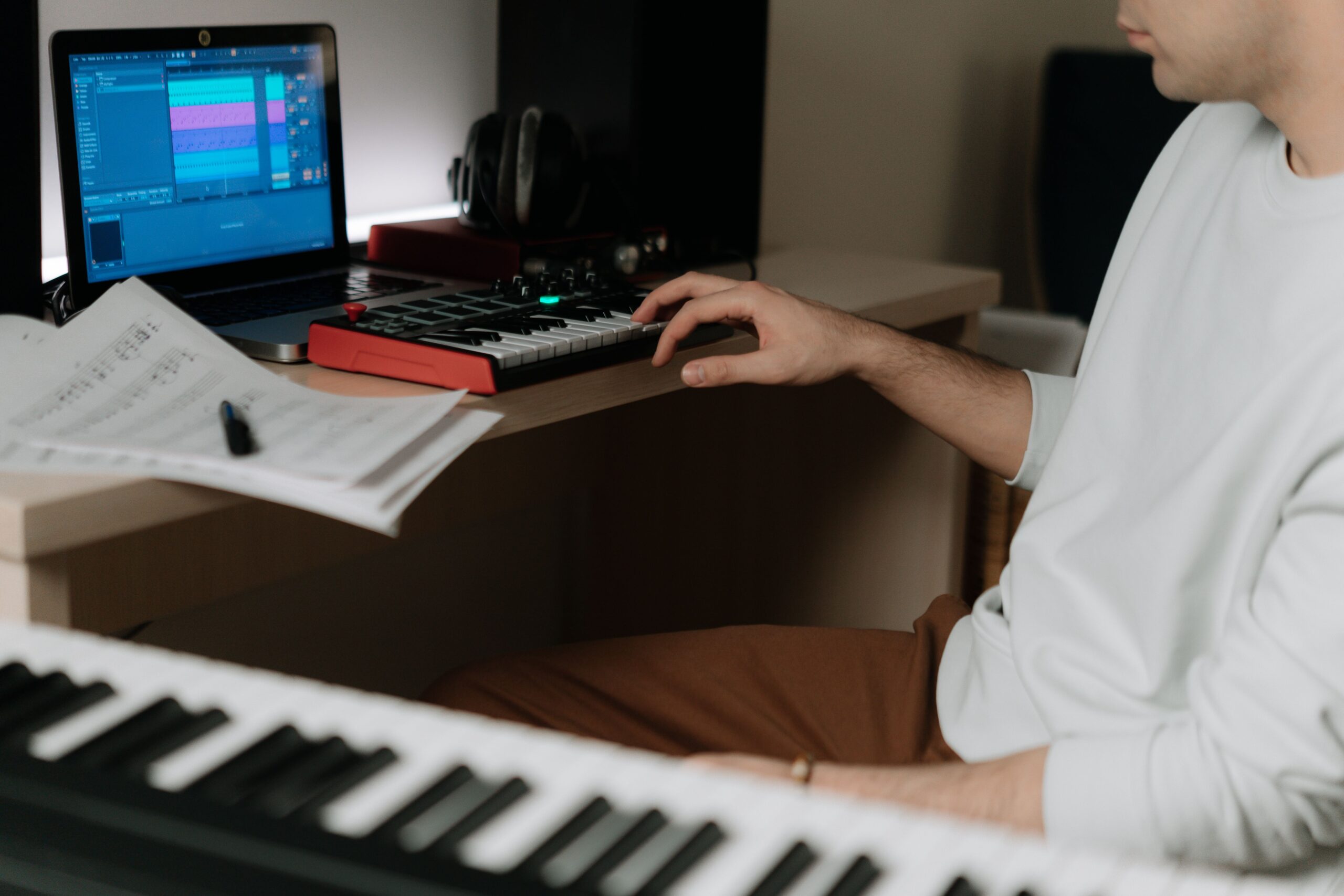 Productor musical utilizando un teclado MIDI y un portátil en un entorno de estudio casero.