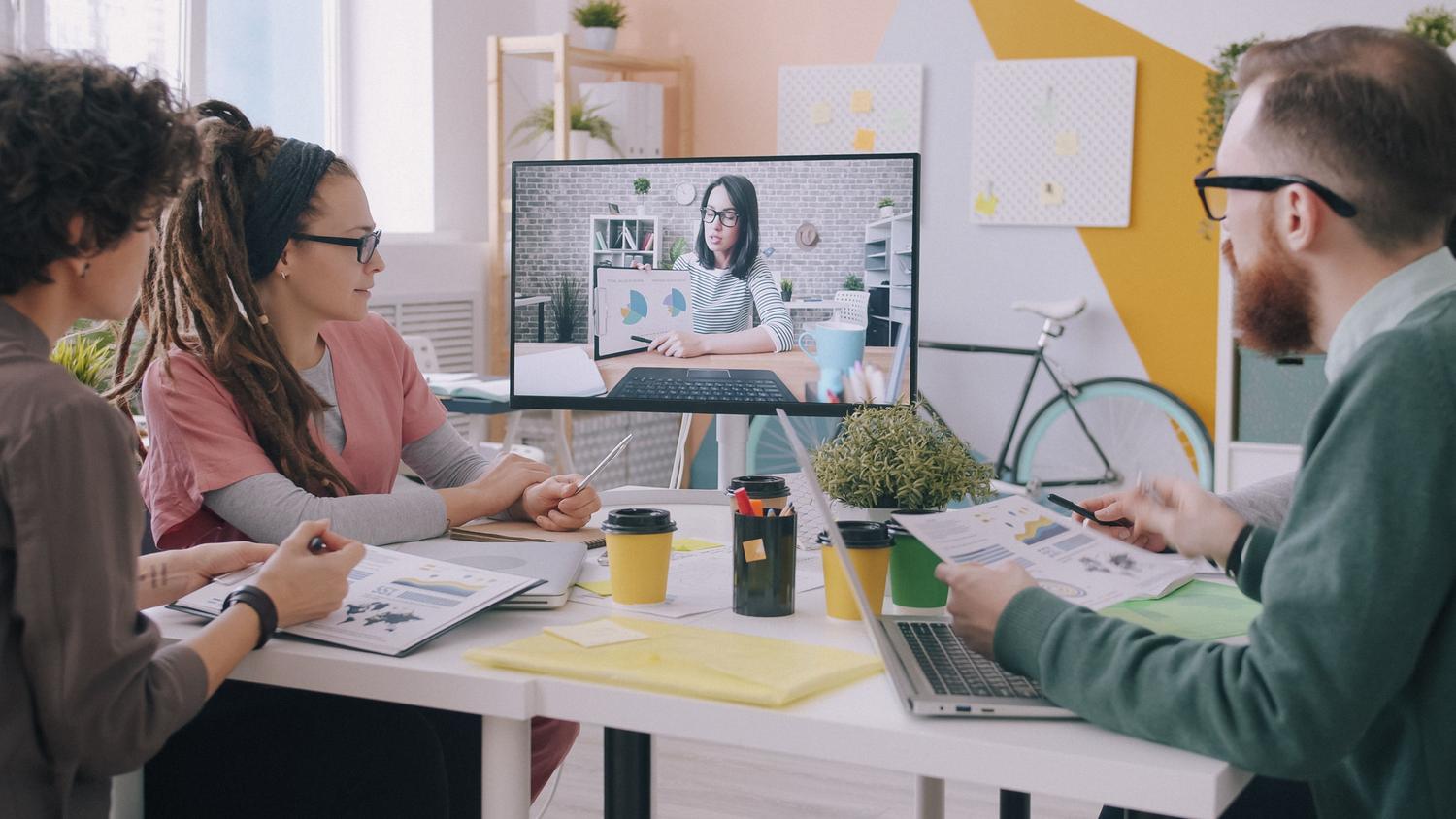 Equipo creativo en una oficina moderna participando en una videoconferencia, reflejando el trabajo remoto y la colaboración en la nube.