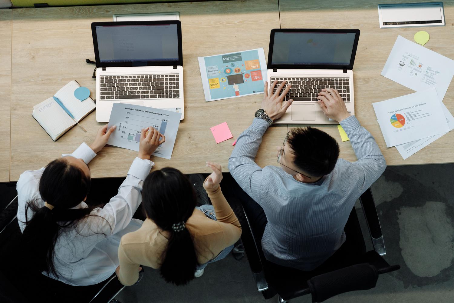Tres colegas trabajando con portátiles y documentos en un escritorio, representando la edición profesional de archivos en equipo.