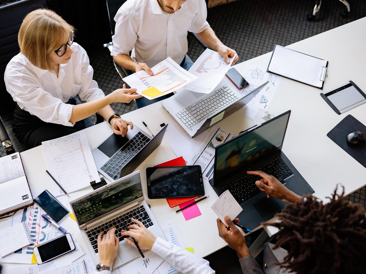 Vista cenital de un equipo de trabajo diverso en una reunión colaborativa con portátiles y papeles, evocando la organización por salas de DocSpace.