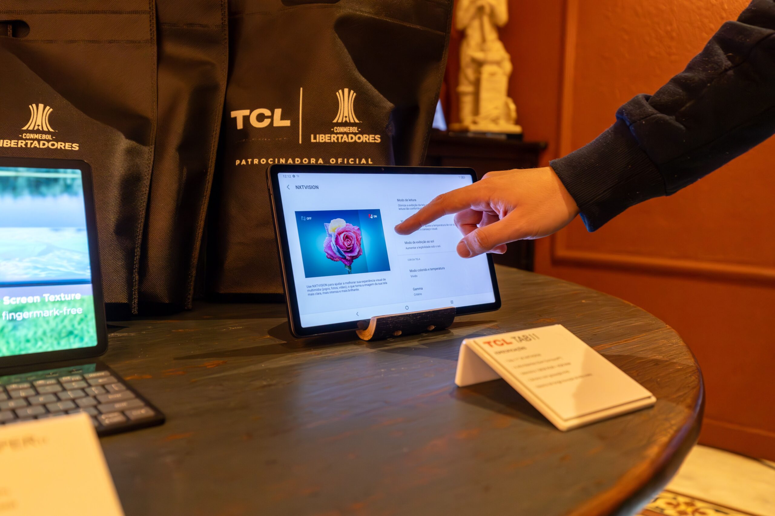Primer plano de una mano tocando una tableta en una exposición de tecnología, representando la interacción táctil.