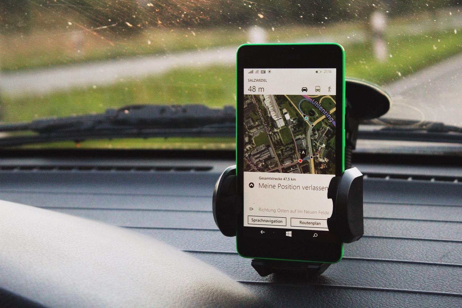 Smartphone con aplicación de GPS montado en el salpicadero de un coche bajo la luz del día, ilustrando el riesgo de sobrecalentamiento.