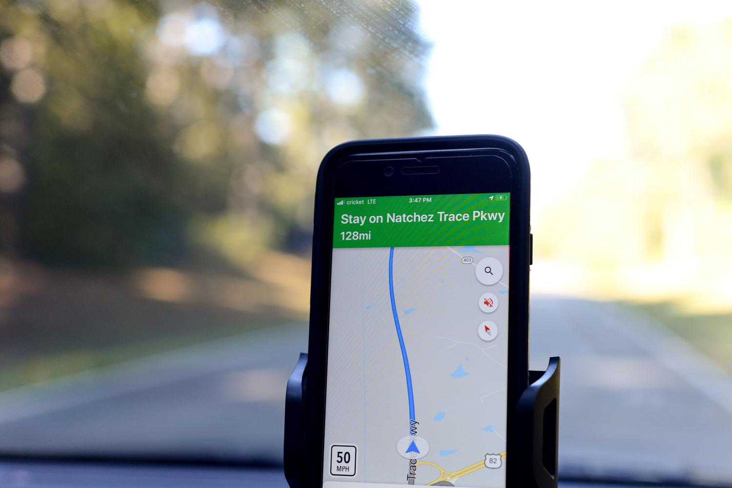 Primer plano de un smartphone mostrando una ruta de navegación GPS en el interior de un vehículo con luz solar intensa.