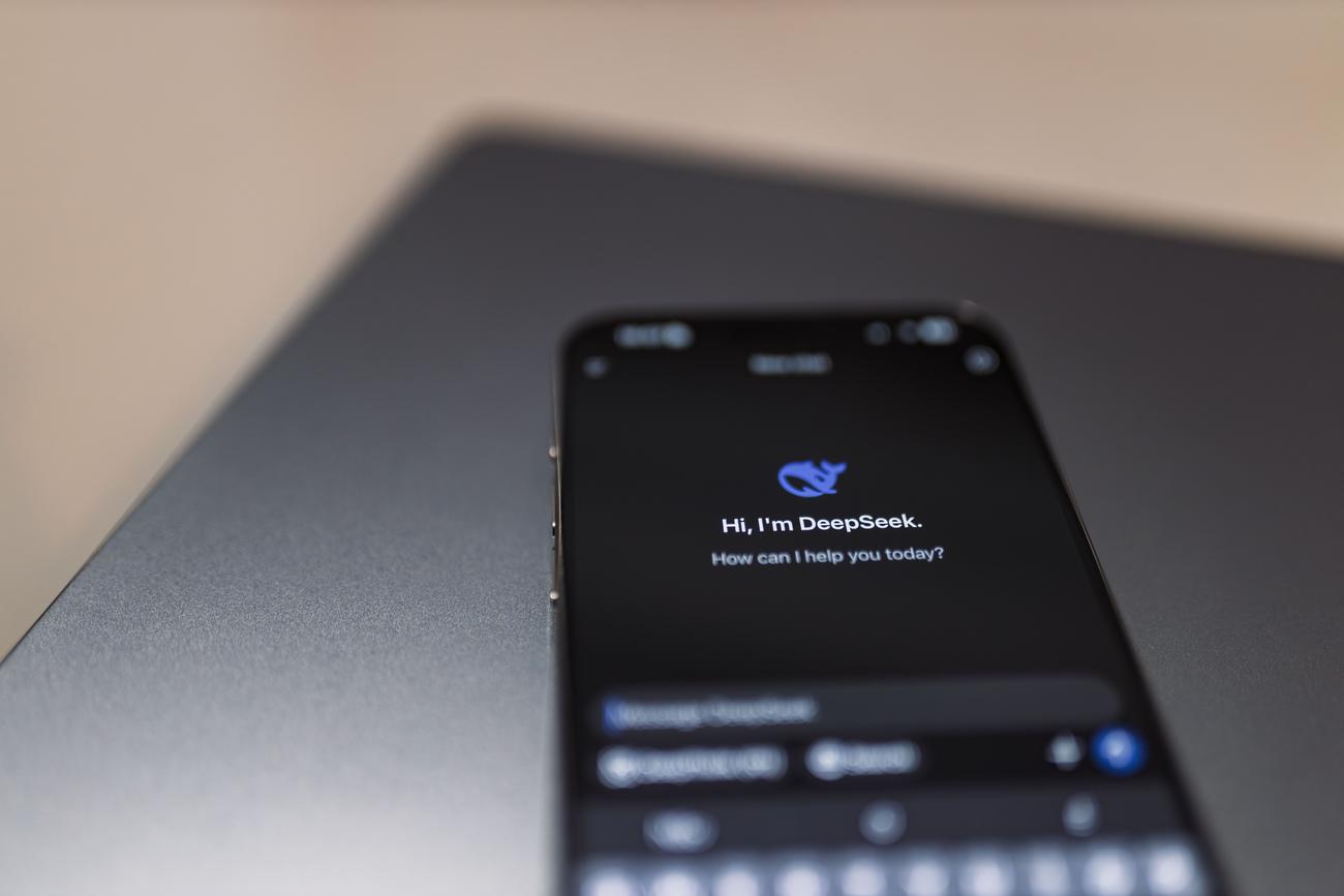 Smartphone mostrando una interfaz de chat de IA con un campo de prompt, apoyado sobre un portátil.